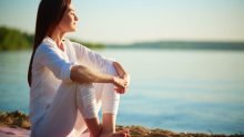 Side view of serene woman sitting on sandy beach against blue sky outdoors